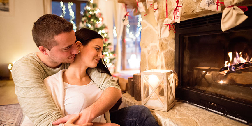 Couple in front of fireplace. Christmas tree behind them.