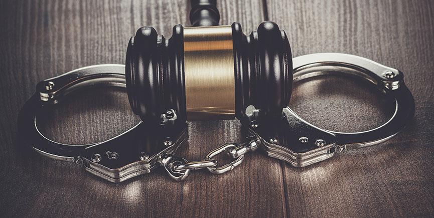 handcuffs and judge gavel on brown wooden table