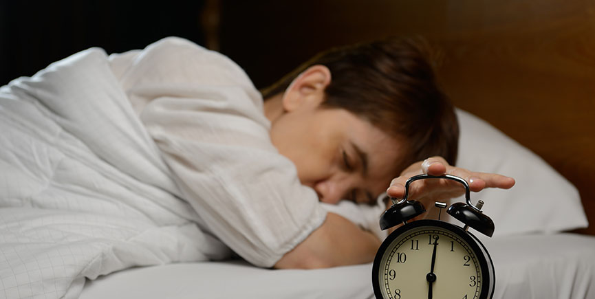 Young woman turning off the alarm clock on the bed